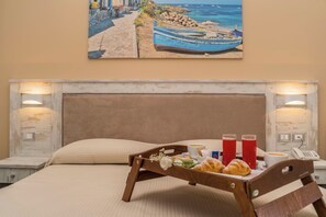 A hotel room with a bed, a tray with food and drinks, a painting of a beach scene, and a telephone on the nightstand.