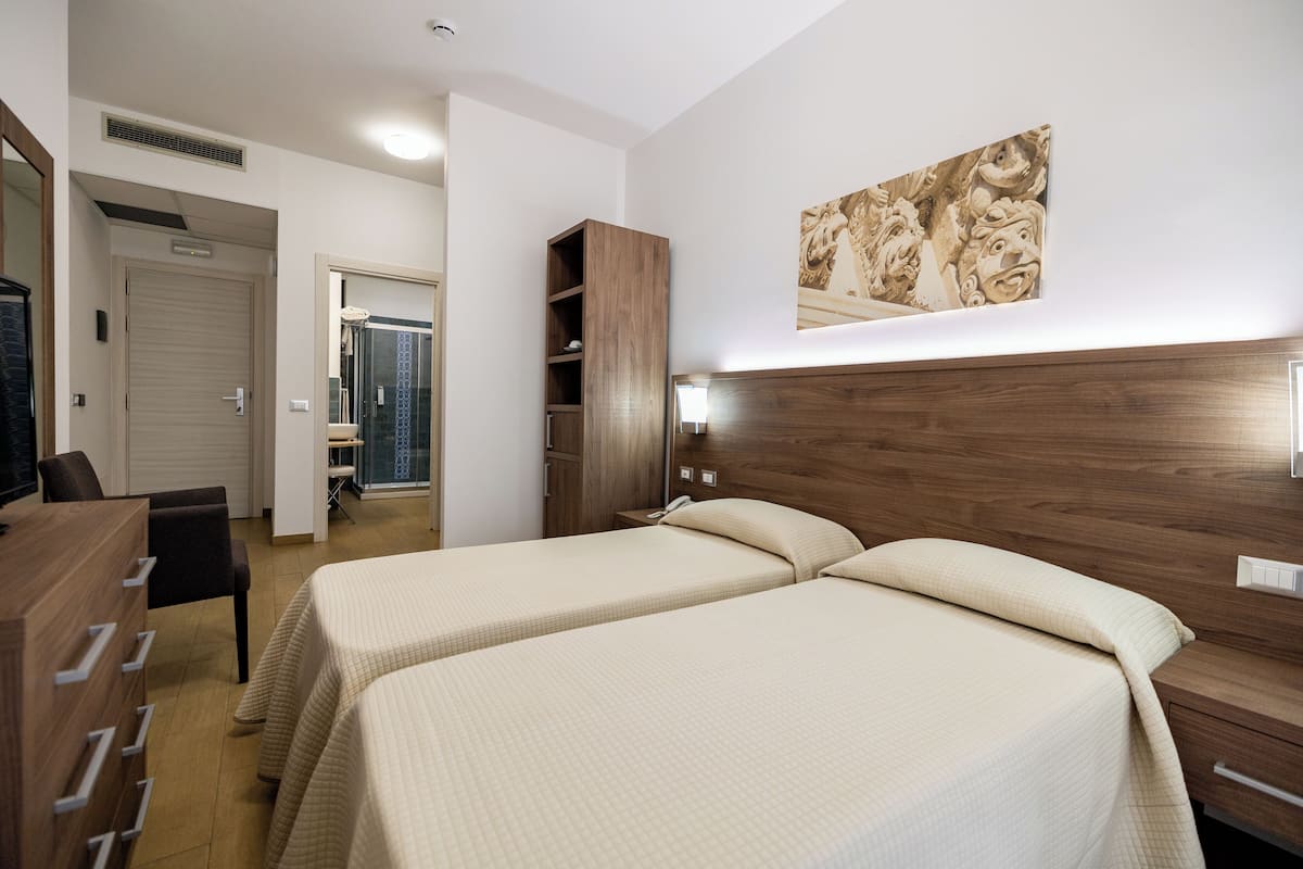 Habitació d'hotel amb dos llits, un panell de capçalera de fusta, un armari i un bany amb dutxa i vàter.