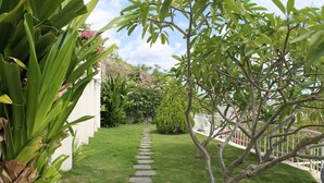 A stone pathway leading through a well-maintained garden with various plants and a white fence. - Casa Mallen - La Boquita (Diriamba)