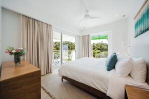 A modern bedroom with a large bed, a wooden nightstand, a vase with flowers, and a view of greenery through the window. - Las Villas Marina Pez Vela (Quepos)