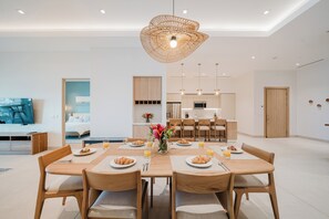 Un espace repas moderne avec une table en bois dressée pour le petit-déjeuner, une cuisine en arrière-plan et un coin salon avec un canapé et un téléviseur.