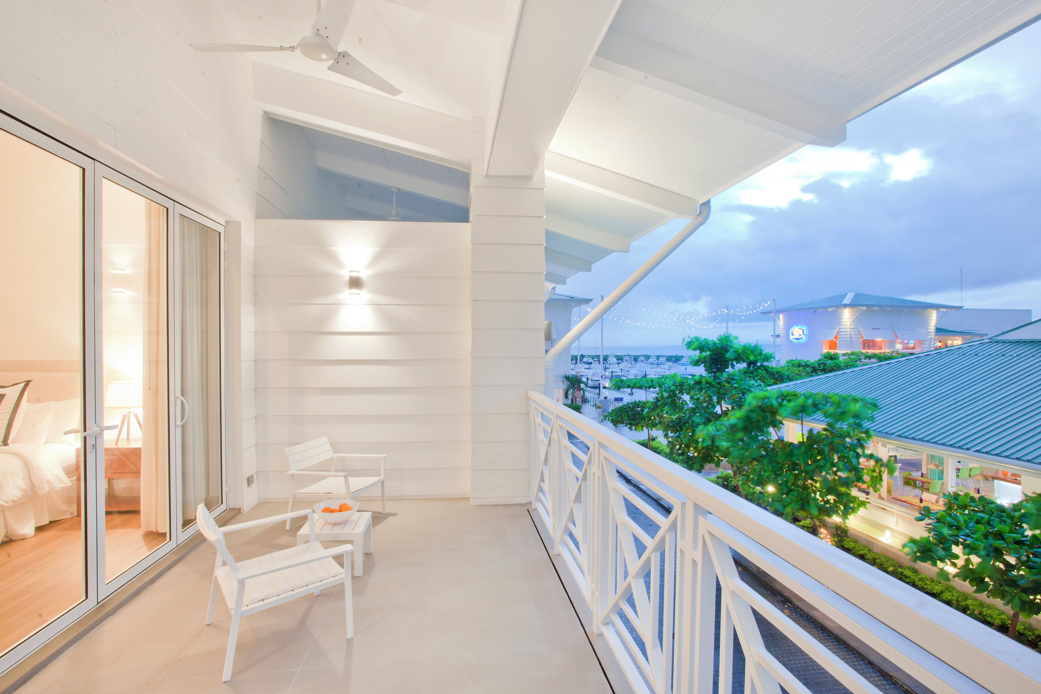 A balcony with a view of a marina, white furniture, and a ceiling fan.