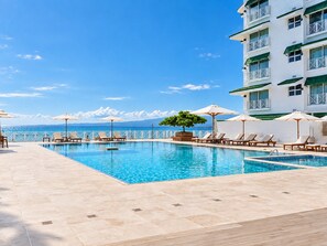 Ein Poolbereich mit Liegestühlen und Sonnenschirmen, bewölkter Himmel und Blick auf den Ozean.