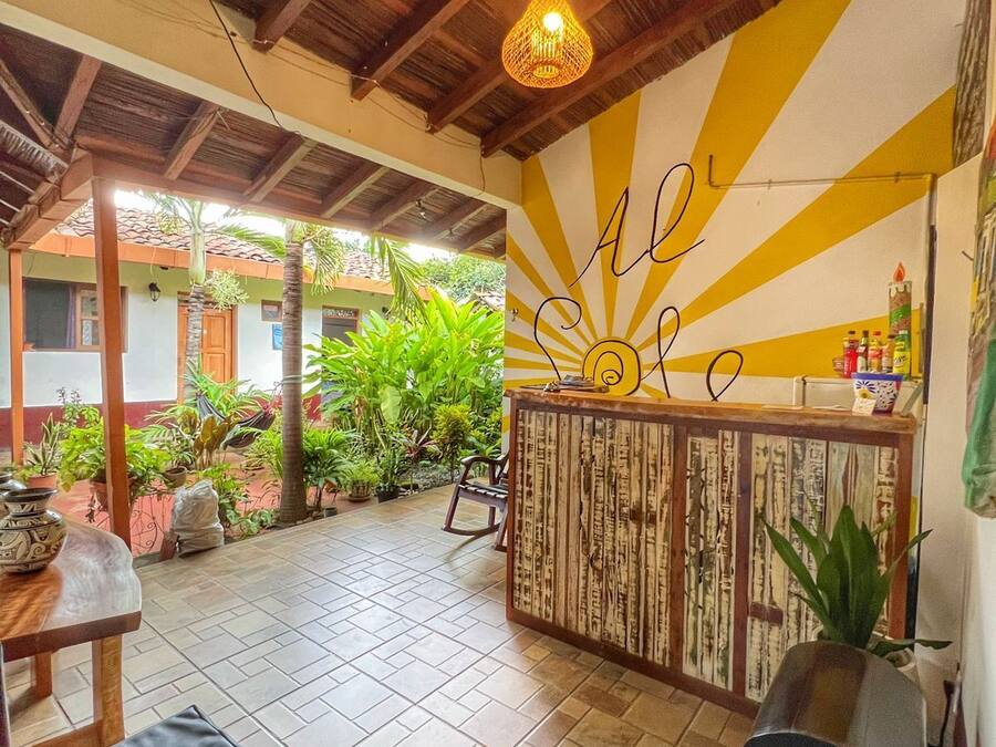 An outdoor patio area with wooden flooring, a central bar with a sun design on the wall, and various plants.