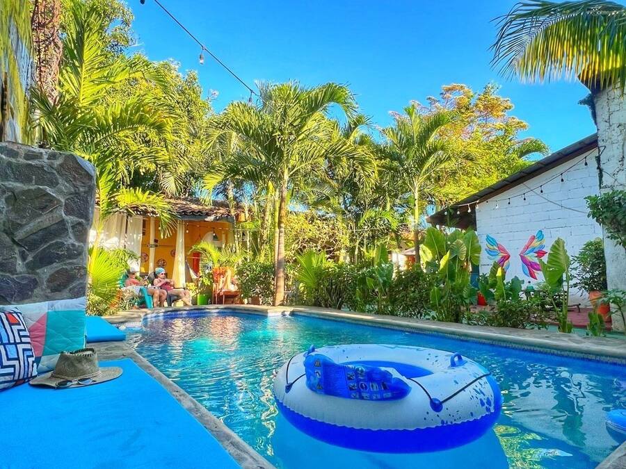 Zona de piscina con un flotador inflable azul, paredes de piedra y plantas tropicales.