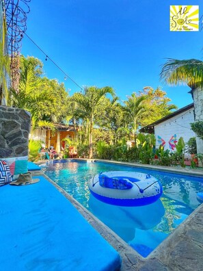 A pool area with a blue inflatable float, stone walls, and tropical plants. - Al Sole Guesthouse (León)
