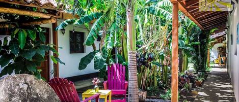 A covered outdoor area with a wooden pergola, a red chair, a yellow table, and a potted plant.