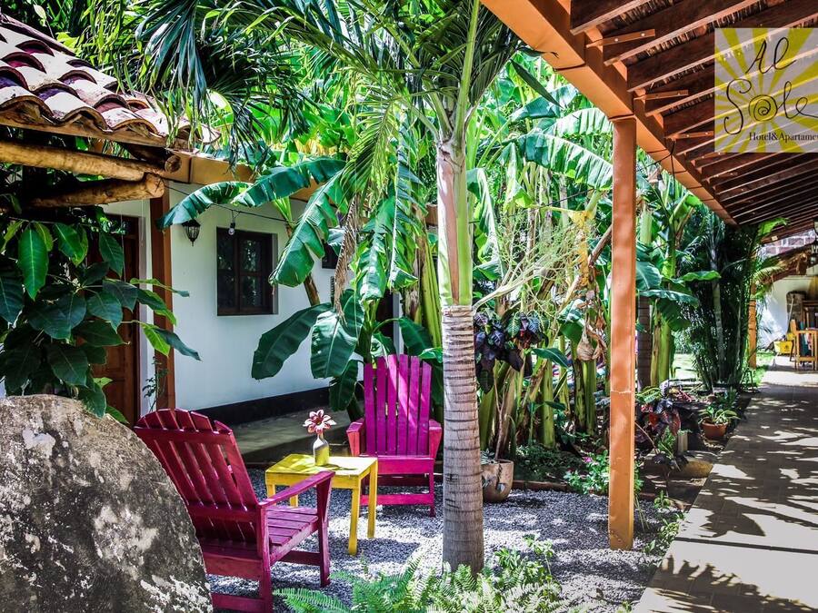 A covered outdoor area with a wooden pergola, a red chair, a yellow table, and a potted plant.