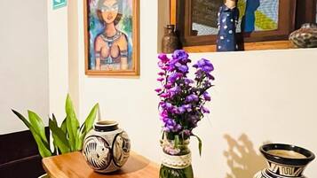 Una mesa de madera con un jarrón de flores moradas, una maceta de cerámica decorativa y un cuadro en la pared.