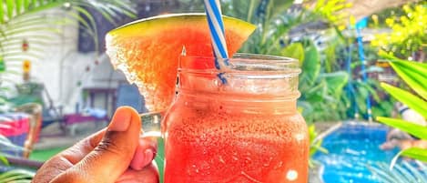 Une main tenant un bocal en verre contenant une boisson rouge et une tranche de pastèque posée sur le bord.