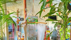 A hammock chair with a patterned cushion, a potted plant, and a sign with various words. - Al Sole Guesthouse (León)