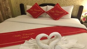 A hotel bed with two pillows labeled "Villa Champa Hotel," a red bedspread, and two swan-shaped towels. - Villa Champa (Luang Prabang)