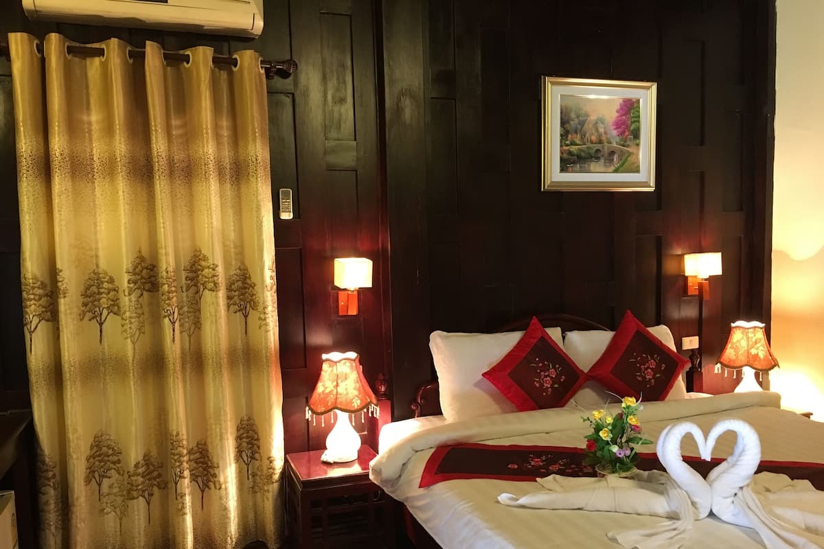 Habitación de hotel con una cama, dos lámparas de noche, una mesita de noche, una cortina y un cuadro en la pared.