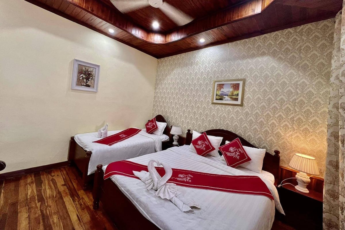 Habitación de hotel con dos camas, techo de madera, papel tapiz estampado y un ventilador de techo.