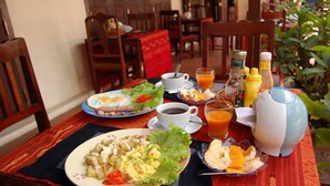 Una mesa de desayuno con platos de comida, tazas de café, vasos de zumo de naranja y aderezos.