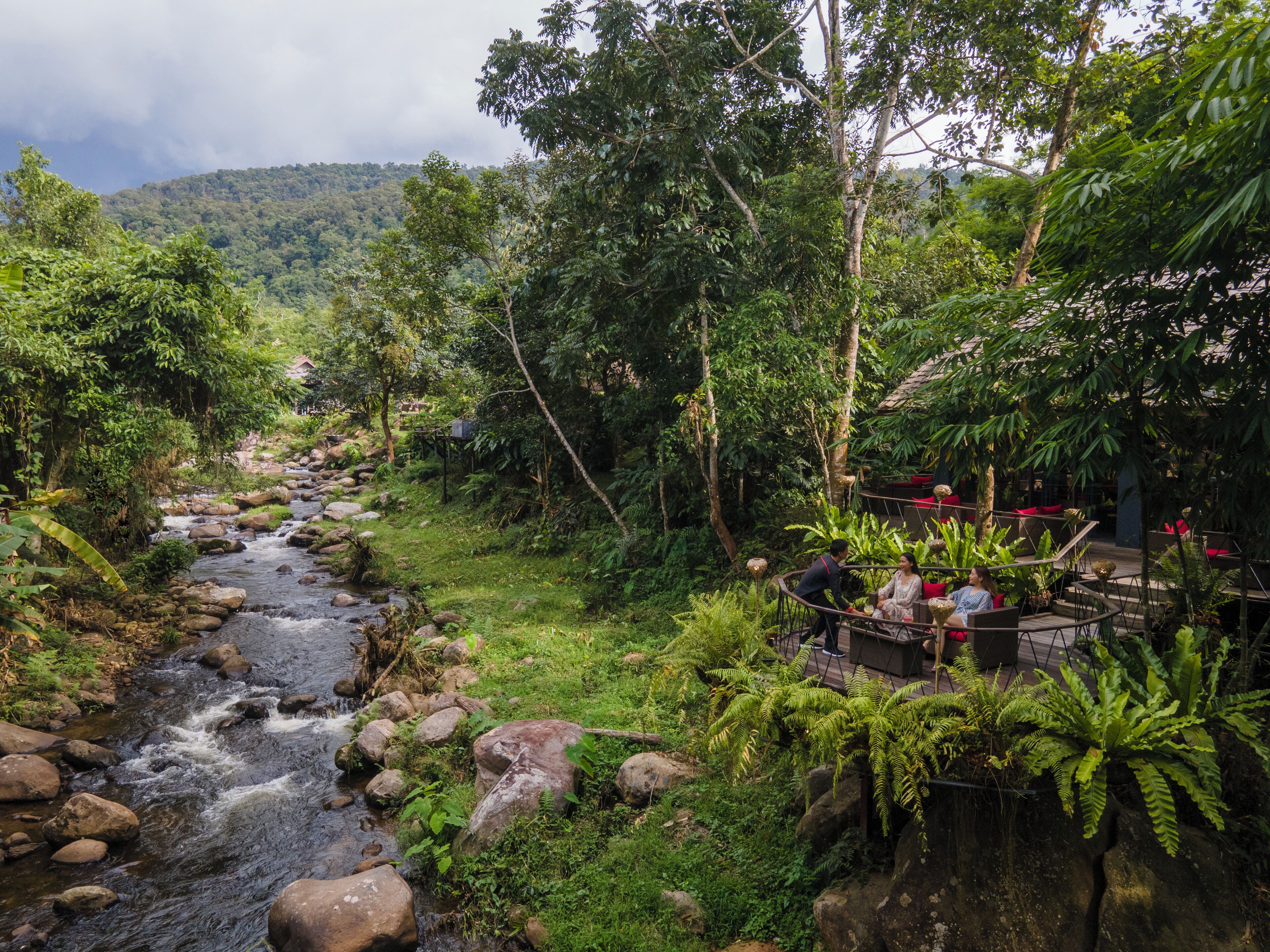 Un jardin luxuriant avec un ruisseau, des espaces de détente en plein air et une vue sur une montagne.
