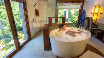 Relax in a serene space with a large bathtub, a wooden bench, and a view of lush greenery.