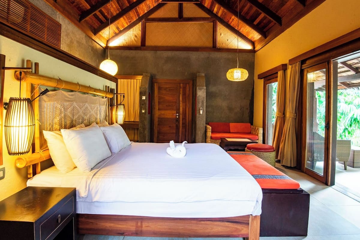 Een slaapkamer met een groot bed, een houten hoofdbord en uitzicht op weelderige begroeiing.