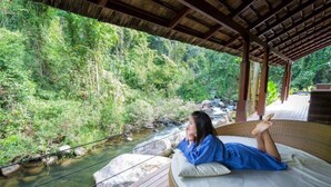 Une personne allongée sur un lit, avec vue sur une rivière et une forêt.