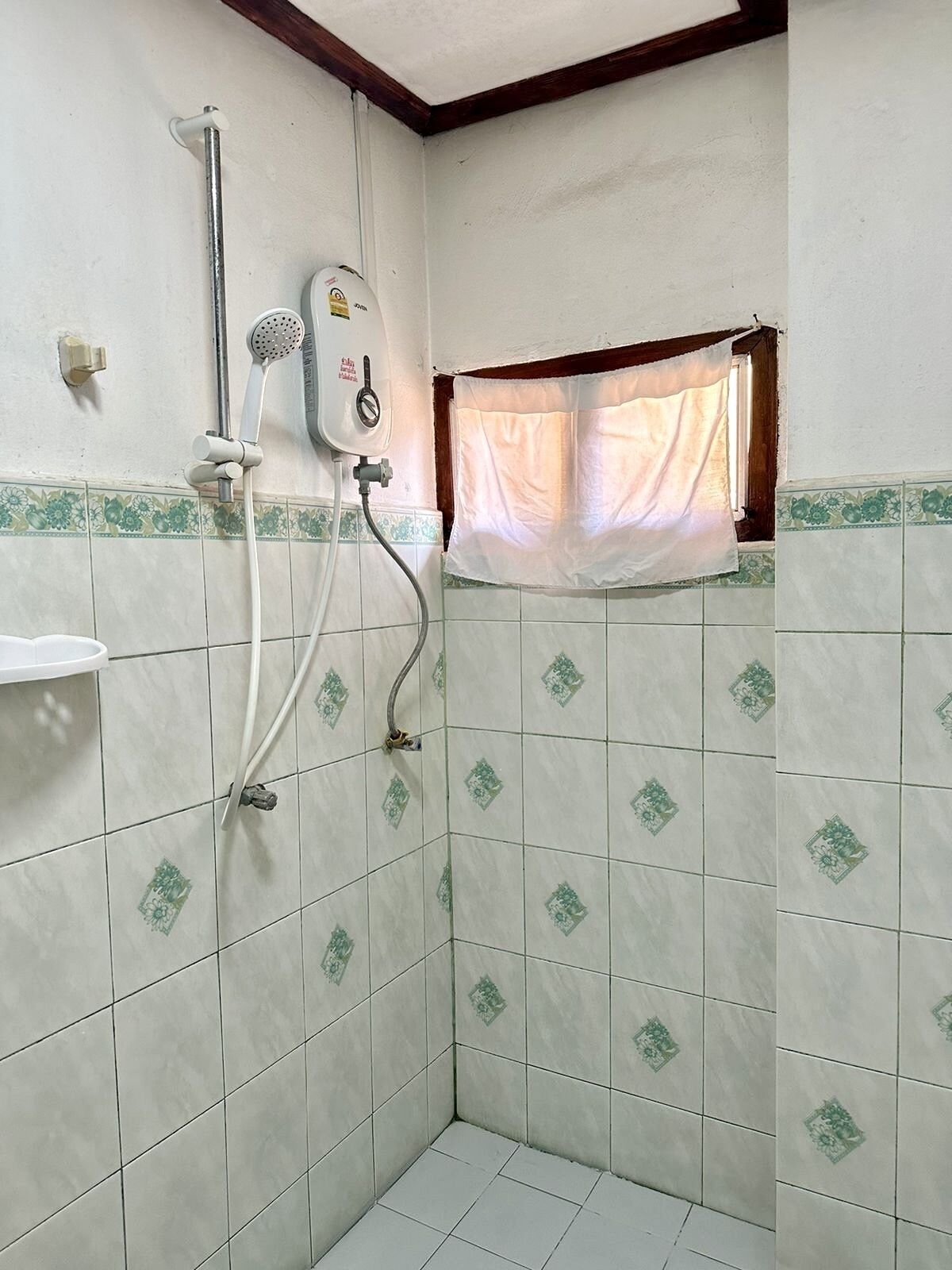 A small bathroom with a shower, a window with a curtain, and decorative tiles.