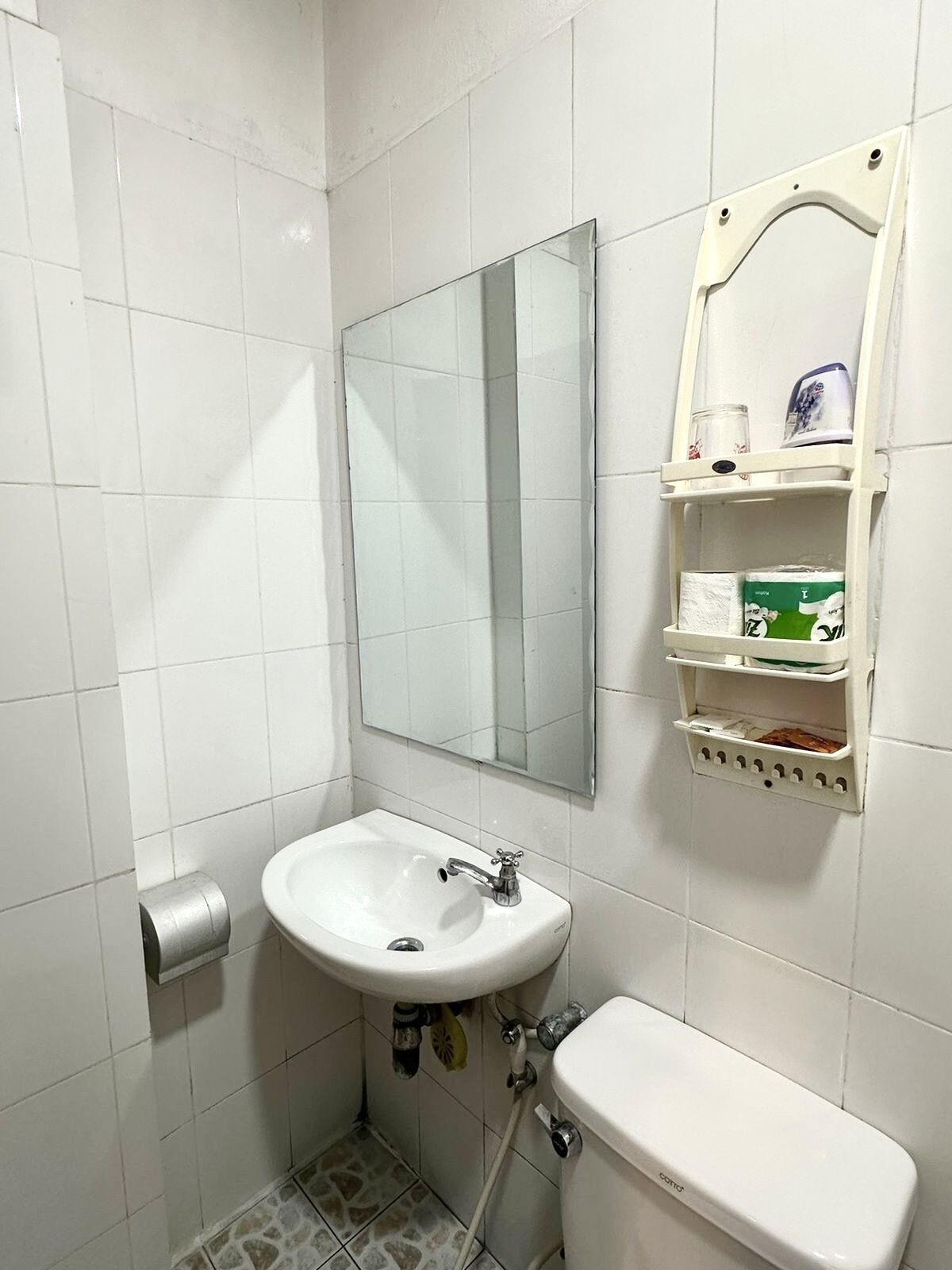 Ein kleines Badezimmer mit einem weißen Waschbecken, einem Spiegel, einer Toilette und einem Ablagefach mit Pflegeartikeln.