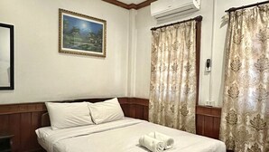 Een netjes opgemaakt bed met een opgerolde handdoek, een ingelijst foto aan de muur en een airconditioning erboven.