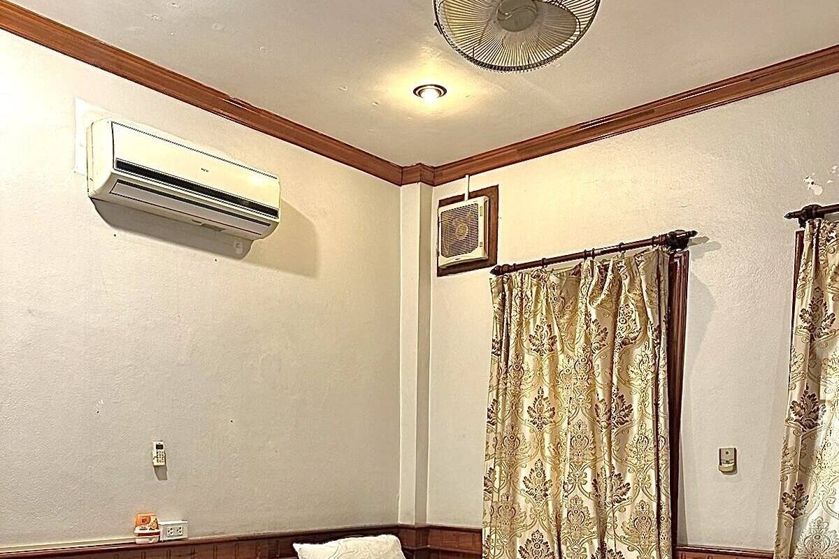 A hotel room with three single beds, a ceiling fan, an air conditioning unit, and a window with curtains.