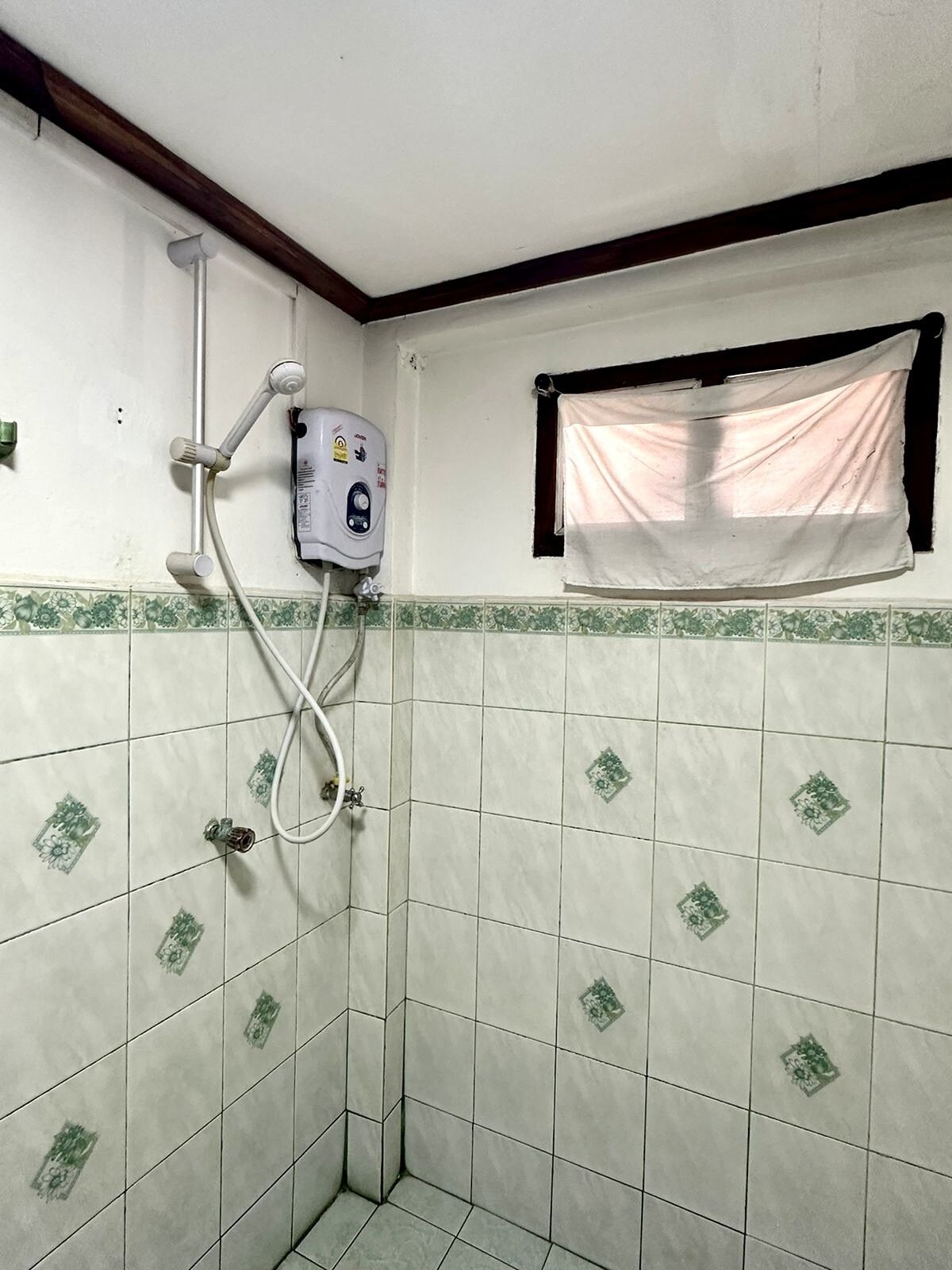 Un baño pequeño con ducha, inodoro y ventana con cortina.