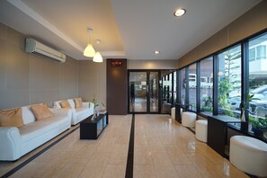 A modern hotel lobby with a reception desk, seating area, and large windows offering views of the outside.