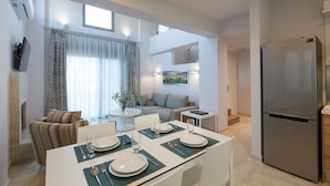 A modern kitchen with a built-in refrigerator, dining table set for four, and a sofa in the adjacent living area. - Eco Villas (Rethymno)
