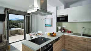 A modern kitchen with a large island, integrated appliances, and a view of a mountainous landscape. - Eco Villas (Rethymno)