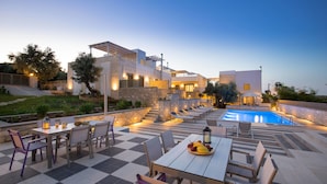 A modern outdoor pool area with a checkered floor, lounge chairs, and a dining table with fruit. - Eco Villas (Rethymno)
