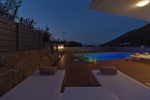 Un área junto a la piscina con sillones de descanso y una pared de piedra.