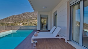 Un área de piscina moderna al aire libre con sillones de descanso, una copa de champán y vistas a un paisaje montañoso.
