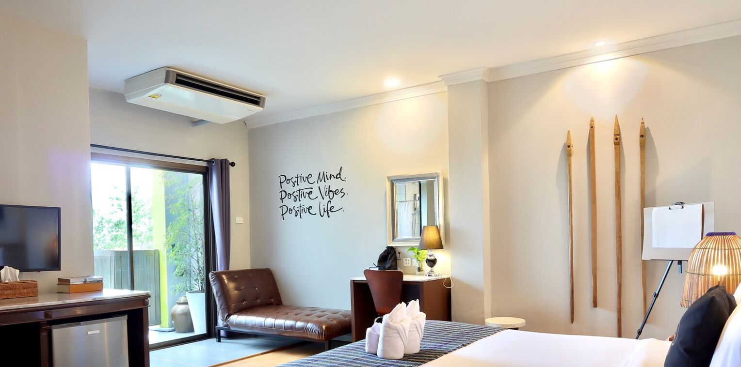 Hotelkamer met een bed, bureau, stoel, televisie, muur met motiverende tekst, raam en uitzicht op groen.