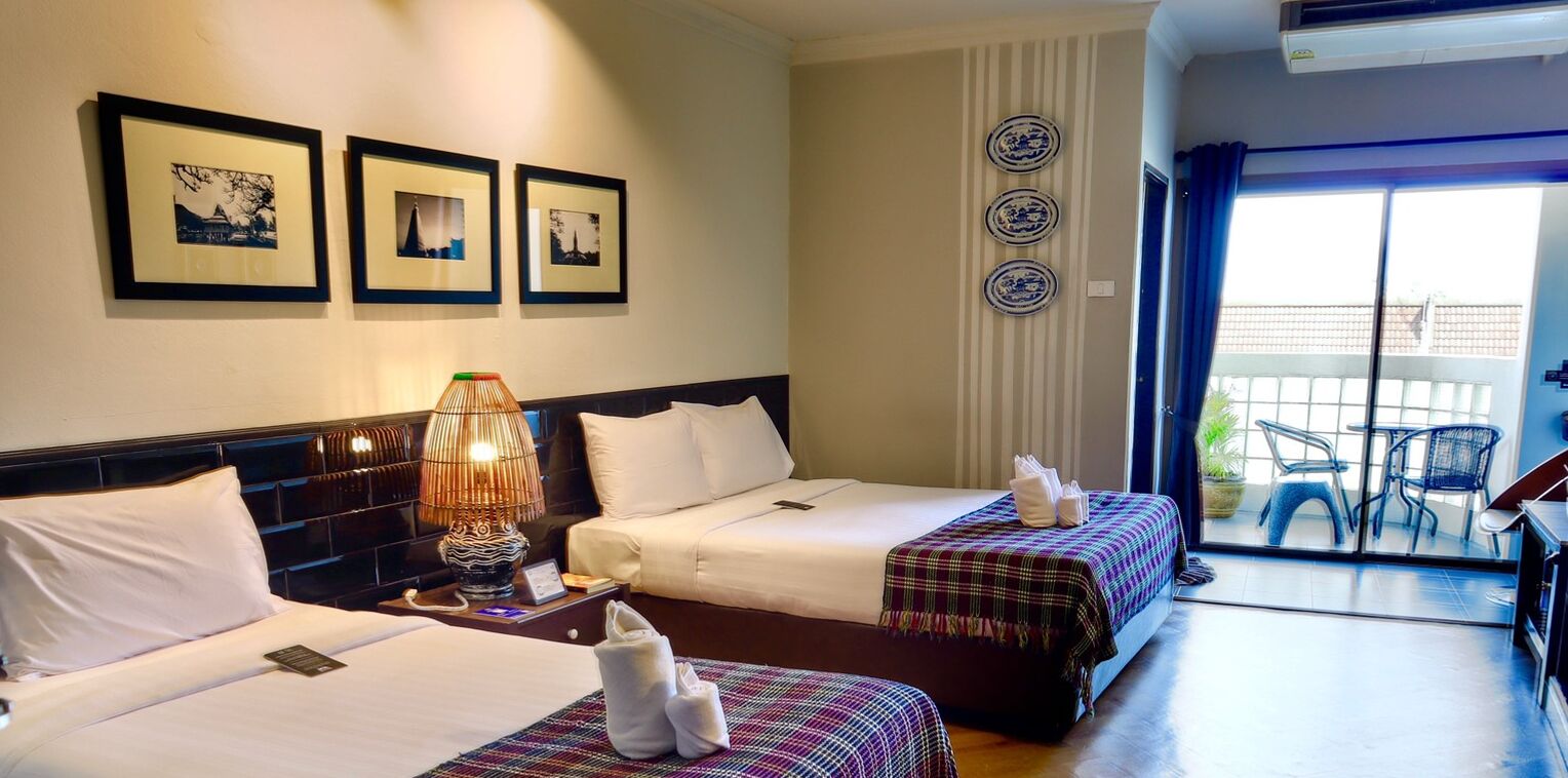 Une chambre d’hôtel avec deux lits, une grande fenêtre avec des rideaux, un balcon avec des chaises et des assiettes décoratives accrochées au mur.
