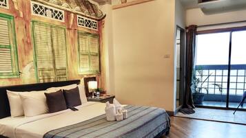 Habitación de hotel con cama, mesita de noche, lámpara, ventana con vistas y puerta al balcón.