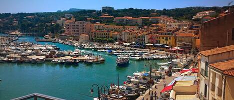A marina with boats docked, a waterfront promenade, and buildings with red-tiled roofs.
