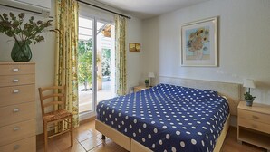 A bedroom with a bed, a chair, a dresser, a nightstand, a lamp, a framed picture, and a window with curtains. - Family Provence Villa in Côte dAzur for 8 (Nans-Les-Pins)