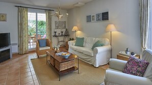 A living room with a white sofa, a coffee table, a TV, and a dining area with chairs and a table. - Family Provence Villa in Côte dAzur for 8 (Nans-Les-Pins)