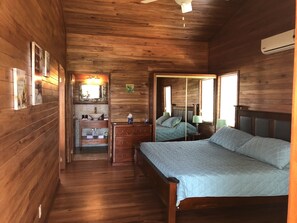 Un dormitorio de cabaña de madera con cama, cómoda, espejo y un pequeño baño.