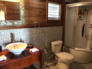 Un baño con tocador de madera, un lavabo blanco, inodoro y cabina de ducha.