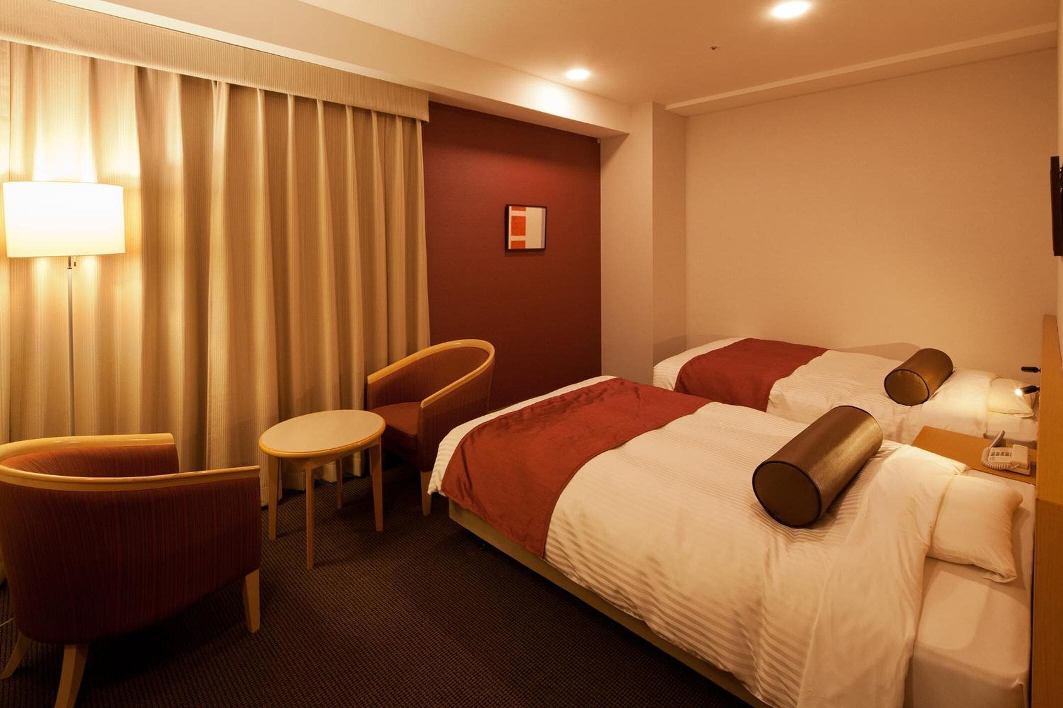 Quarto de hotel com duas camas, uma mesa, uma cadeira e um abajur.