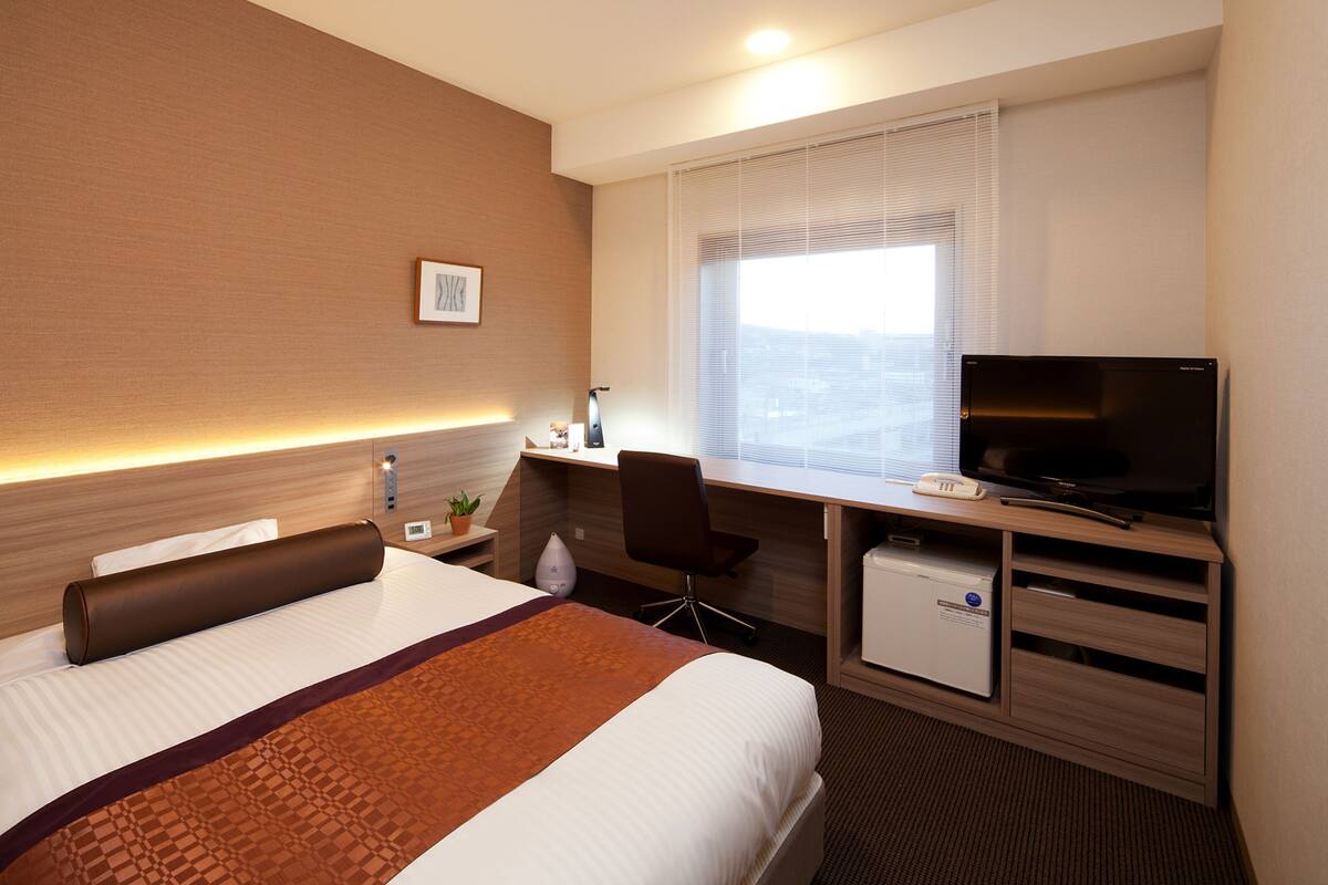 A hotel room with a bed, desk, television, and a small refrigerator.