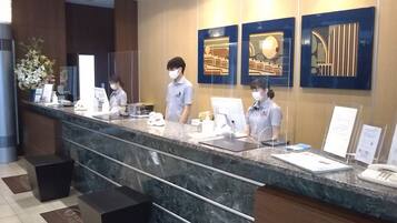 A reception desk with a marble counter, two receptionists, and a large decorative mirror.