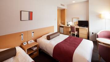 A hotel room with two beds, a desk, a chair, a TV, and a small kitchenette.