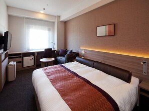 A hotel room with a large bed, a desk with a chair, a small table, and a sofa.
