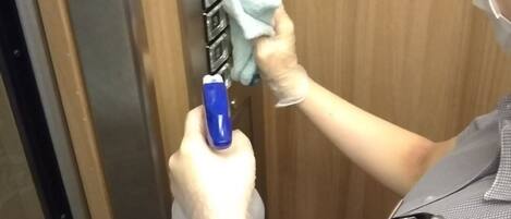 A person cleaning an elevator door with a spray bottle and cloth.