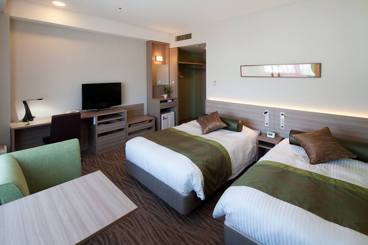 A hotel room with two beds, a desk with a television, a chair, and a small table.