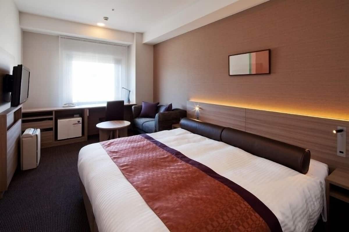 A hotel room with a large bed, a desk with a chair, a small table, and a sofa.